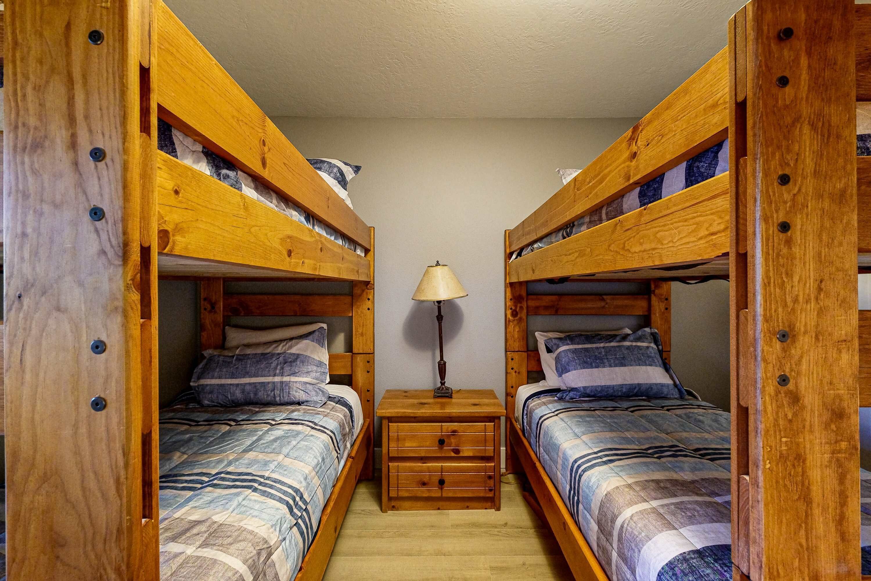 A room with two bunk beds, a wooden nightstand with drawers, and a table lamp.