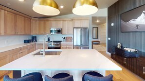 Une cuisine moderne dotée de meubles en bois, d’appareils électroménagers en acier inoxydable, d’un îlot central et de luminaires suspendus.