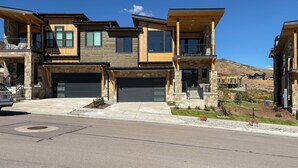 A modern multi-story residential building with a garage, large windows, and a balcony. - Panoramic views, hot tub & game room, Minutes from Jordanelle Express Gondola (Heber City)