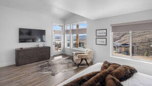 A modern bedroom with a large window, a flat-screen TV, and a view of a mountainous landscape. - Panoramic views, hot tub & game room, Minutes from Jordanelle Express Gondola (Heber City)