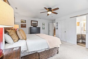 A bedroom with a bed, a ceiling fan, a dresser, and a door leading to a bathroom. - Stylish condo in prime location just steps from Main Street & Town Lift Plaza (Park City)