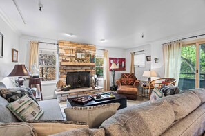 A living room with a stone fireplace, a sofa, a coffee table, and a view of the outdoors. - Stylish condo in prime location just steps from Main Street & Town Lift Plaza (Park City)