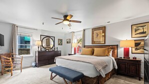 Ein Schlafzimmer mit Bett, einer Bank, einem Schminktisch und einem Deckenventilator.