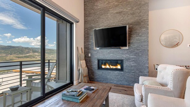 Ein modernes Wohnzimmer mit Kamin, großem Fernseher und einem Balkon mit Bergblick.
