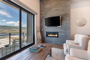 Ein modernes Wohnzimmer mit Kamin, großem Fernseher und einem Balkon mit Bergblick.