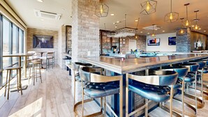 Un espace bar doté de nombreux tabourets, d’un long comptoir et de luminaires suspendus.