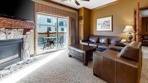 A living room with a sofa, coffee table, TV, ceiling fan, and a view of a balcony with outdoor furniture. - ski-in ski-out Condo with Shared Hot Tubs & Pool, High-Speed WiFi, and Central AC (Park City)