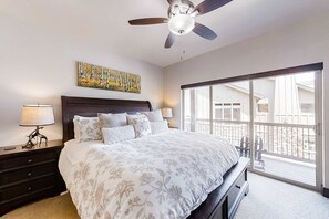 Ein Schlafzimmer mit einem großen Bett, einem Deckenventilator, einem Nachttisch mit Lampe, einem Bild an der Wand und einem Balkon mit Aussicht.