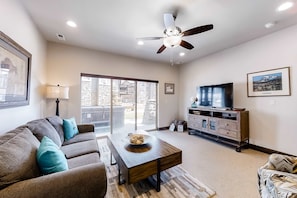 A living room with a sofa, coffee table, TV, and ceiling fan. - Spacious, new-build stunner near Park City & Deer Valley with private hot tub (Kamas)
