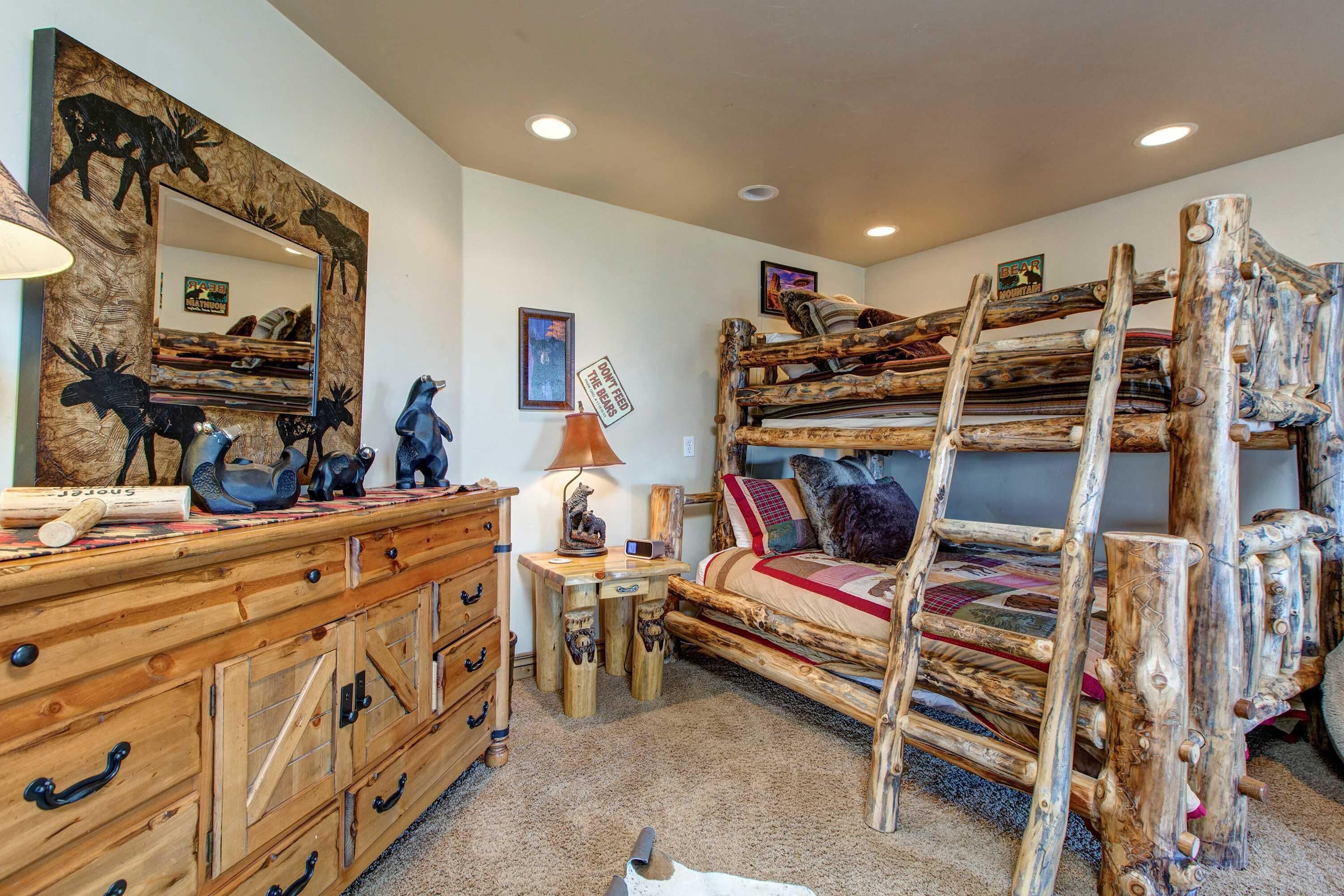 Ein rustikales Schlafzimmer mit einem Holzkasten, einem Spiegel mit Tiermotiven, einem Etagenbett und einem kleinen Schreibtisch mit Lampe.
