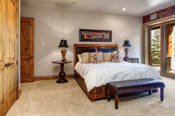 A bedroom with a large bed, two bedside tables, a bench, a door, and a window.