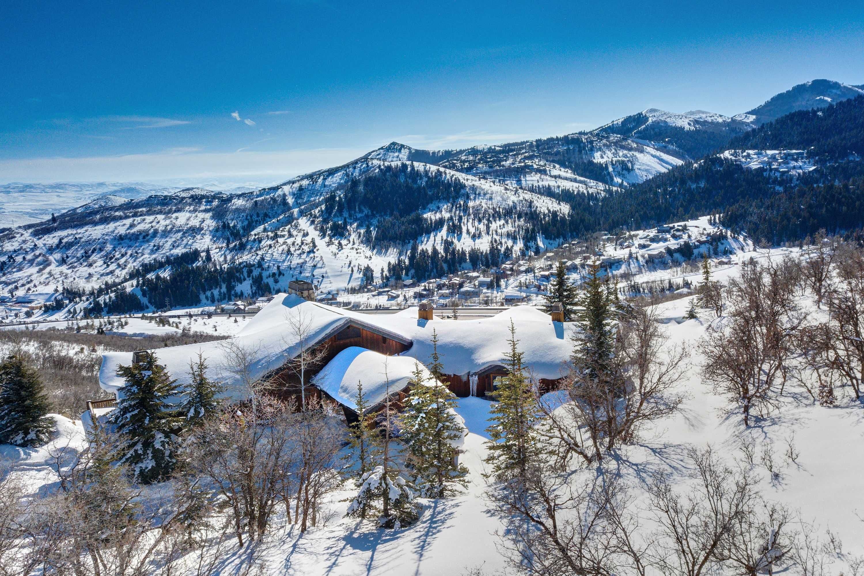 Una cabaña de montaña con techos nevados, rodeada de árboles y montañas.