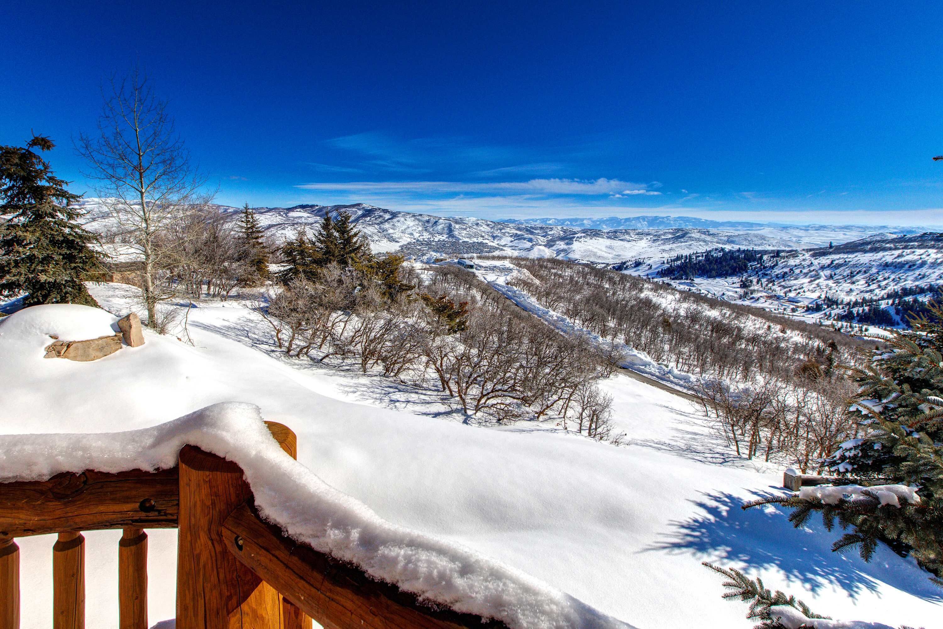 A snow-covered landscape with a wooden deck and a view of distant mountains.
