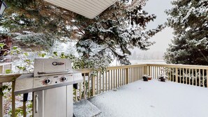 A covered outdoor area with a barbecue grill, a wooden deck, and snow-covered trees. - Three-story townhome with fireplace & decks - steps to shuttle & rec center (Park City)