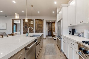 Une cuisine moderne avec des meubles blancs, des appareils en acier inoxydable et des luminaires suspendus.