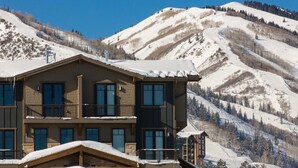 Un hotel de varios pisos con un balcón, con una imponente montaña nevada al fondo.