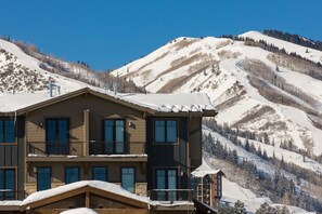 Ein mehrstöckiges Hotel mit Balkon vor einer verschneiten Berglandschaft.
