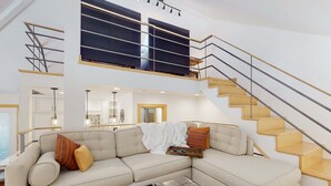 Una sala moderna con un sofá modular, una mesa de centro y una escalera con barandilla.