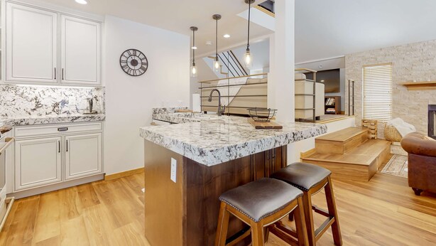 Una cocina moderna con una isla de mármol, taburetes de madera y una escalera que lleva a un altillo.