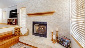 Una chimenea de piedra con fuego, un banco de madera, una cesta y un mueble para revistas.