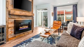 A modern living room with a fireplace, a flat-screen TV, a dining area, and a large window. - Private Rooftop Hot Tub Views Bumper Pool Table, High-Speed WiFi & Fireplace (Park City)