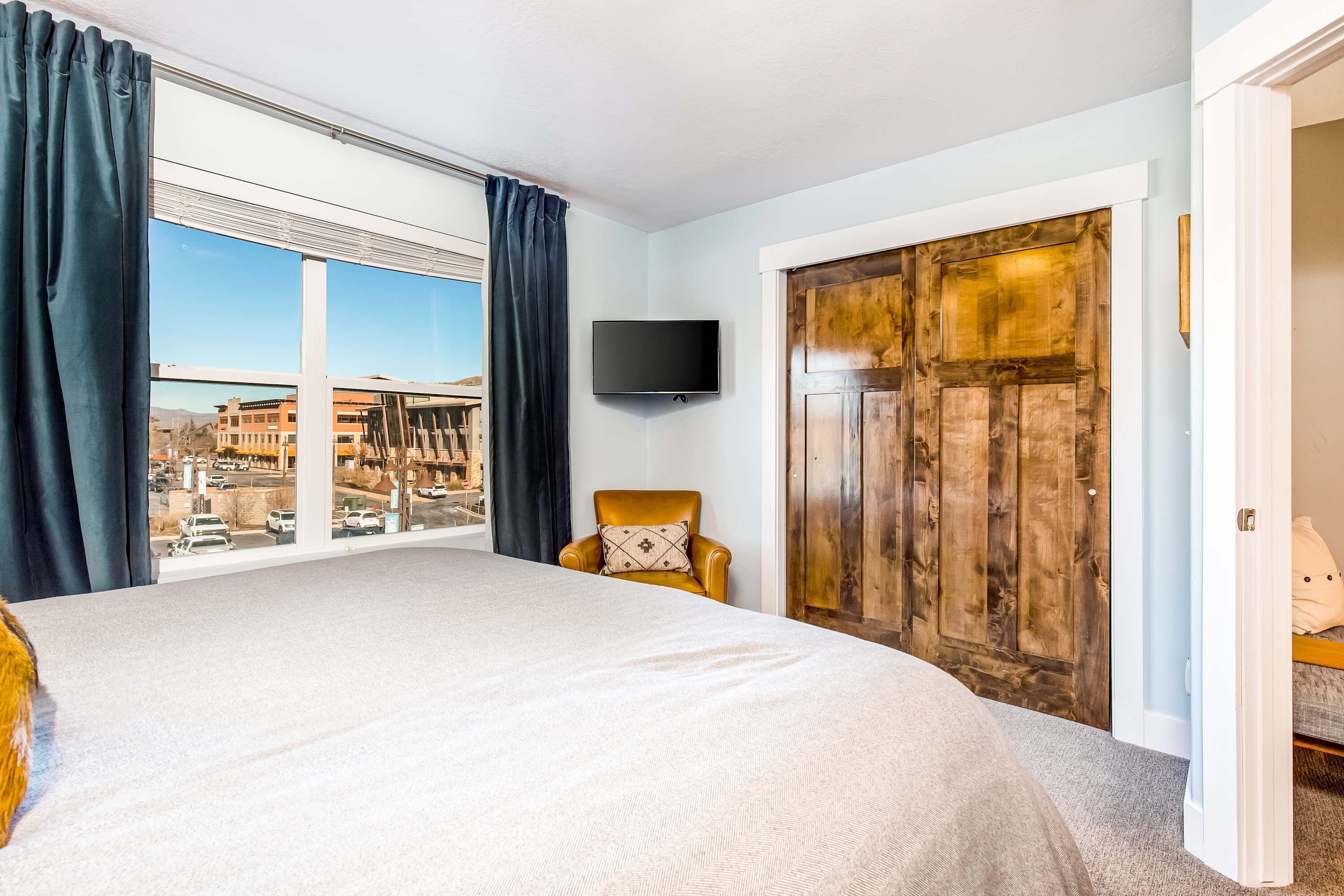 Ein Schlafzimmer mit einem großen Bett, einem Sessel, einem Fernseher und Blick auf die Stadt.