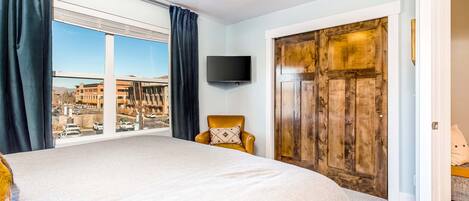 Ein Schlafzimmer mit einem großen Bett, einem Sessel, einem Fernseher und Blick auf die Stadt.
