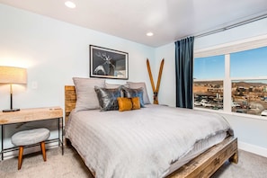 Une chambre à coucher avec un lit, un bureau, une chaise, une fenêtre donnant sur un beau paysage et un tableau accroché au mur.