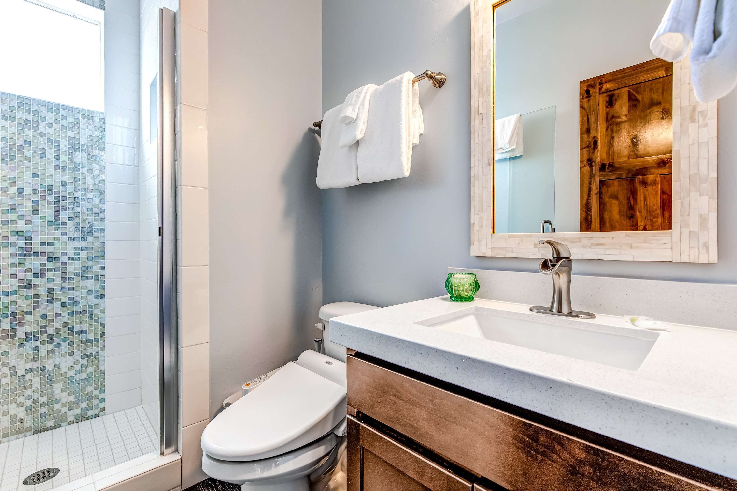 A bathroom with a shower, toilet, sink, and a mirror.