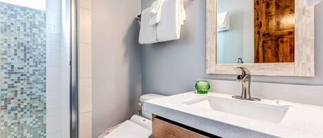 A bathroom with a shower, toilet, sink, and a mirror.