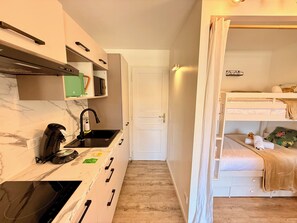 Eine kompakte Küche mit Kaffeemaschine, Mikrowelle und Spüle. Eine weiße Tür führt zu einem Schlafzimmer mit Etagenbett.