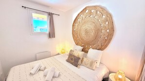 Ein Schlafzimmer mit Bett, Kissen, Wandbild, Fenster und Nachttischlampe.
