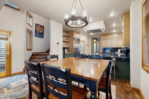 Ein Essbereich mit Holztisch und -stühlen, einer Chandelüstere und einer Küche im Hintergrund.