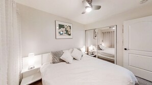 Ett hotellrum med en säng, sänglampor, en takfläkt, en spegel och en dörr.