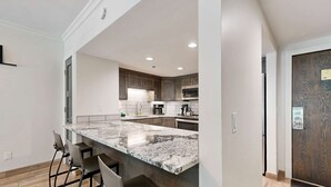 A modern kitchen with a marble countertop, dark wooden cabinets, and a bar seating area. - Fully Renovated Condowith Patio, Wood Fireplace & Hot Tub (Park City)