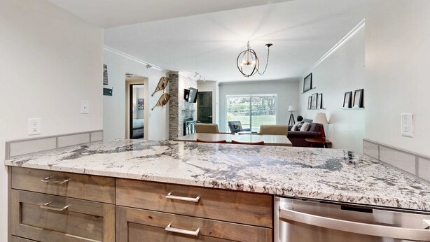A kitchen with a marble countertop, wooden cabinets, a dishwasher, and a dining area with a table and chairs. - Fully Renovated Condowith Patio, Wood Fireplace & Hot Tub (Park City)