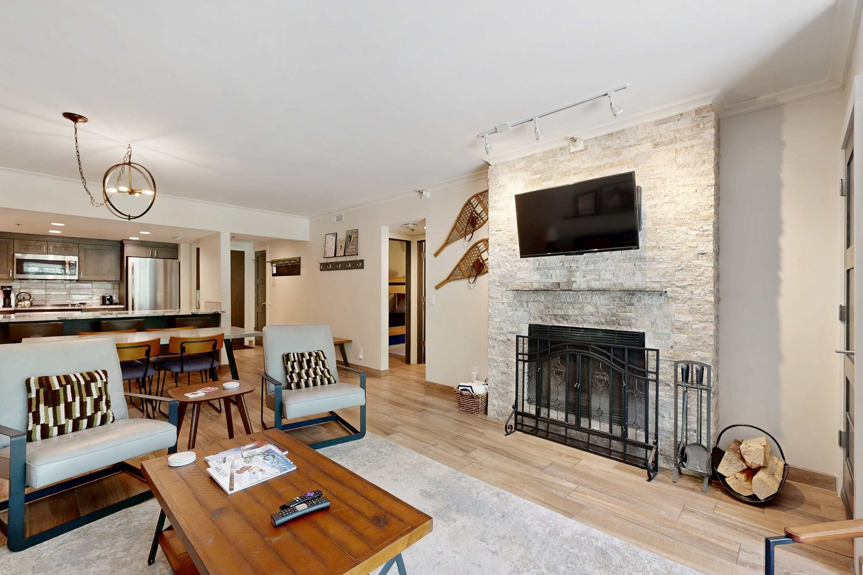 A modern living room with a fireplace, a television mounted on the wall, and a dining area with chairs and a table.