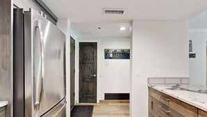 A kitchen with a stainless steel refrigerator, wooden cabinets, a marble countertop, and a wooden door. - Fully Renovated Condowith Patio, Wood Fireplace & Hot Tub (Park City)