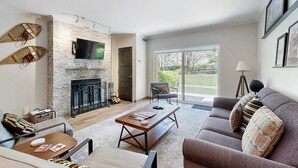 A living room with a fireplace, a sofa, a coffee table, and a television. - Fully Renovated Condowith Patio, Wood Fireplace & Hot Tub (Park City)