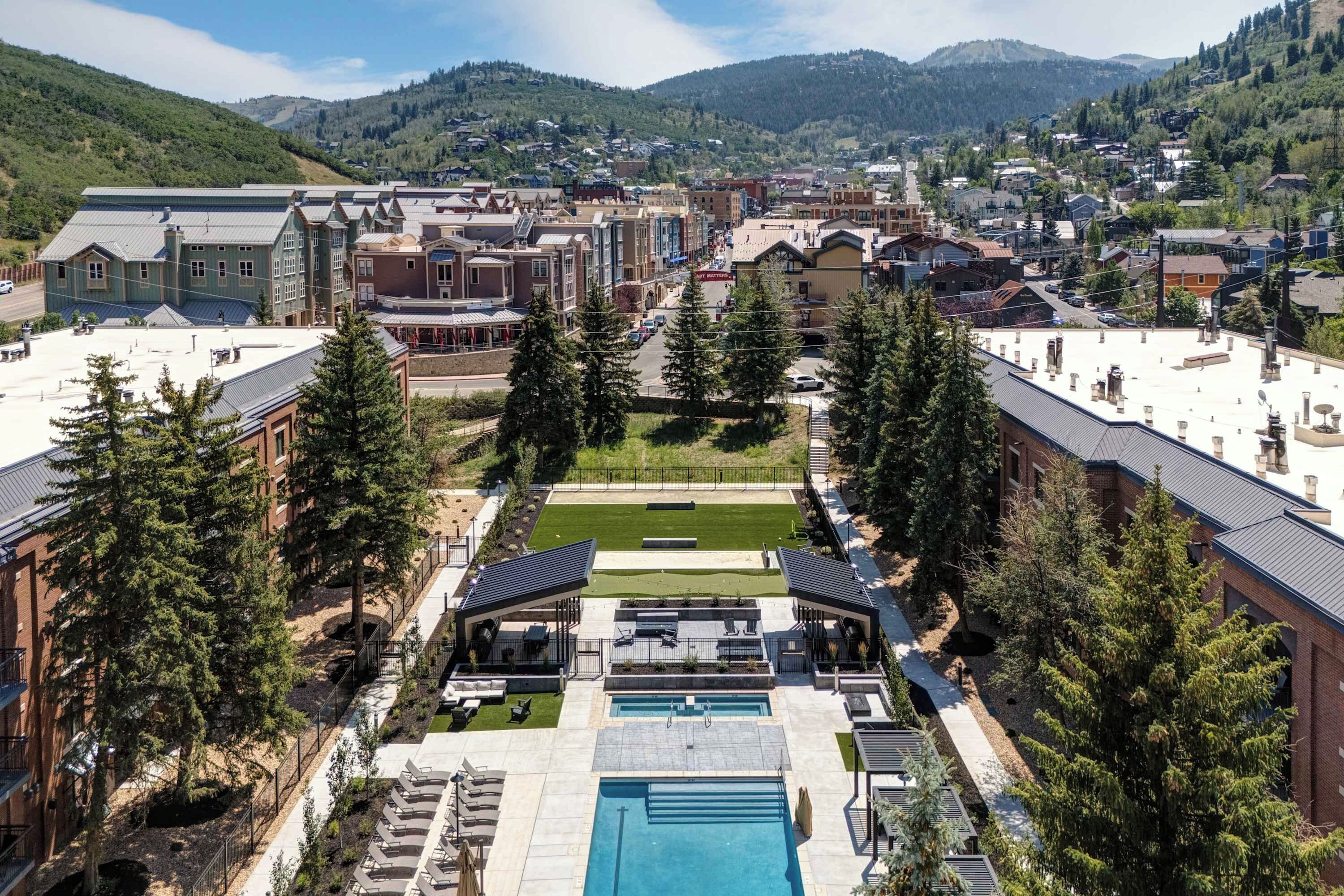 A hotel with a swimming pool, outdoor seating, and a view of the surrounding town and mountains.