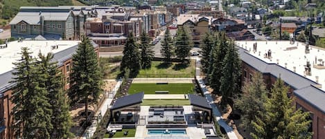 Un hotel con piscina, mobiliario exterior y vistas del pueblo y las montañas circundantes.