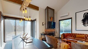 Ein modernes Wohnzimmer mit einem großen Holzesstisch, Ledersofas, einem Kamin und einem an der Wand befestigten Fernseher.