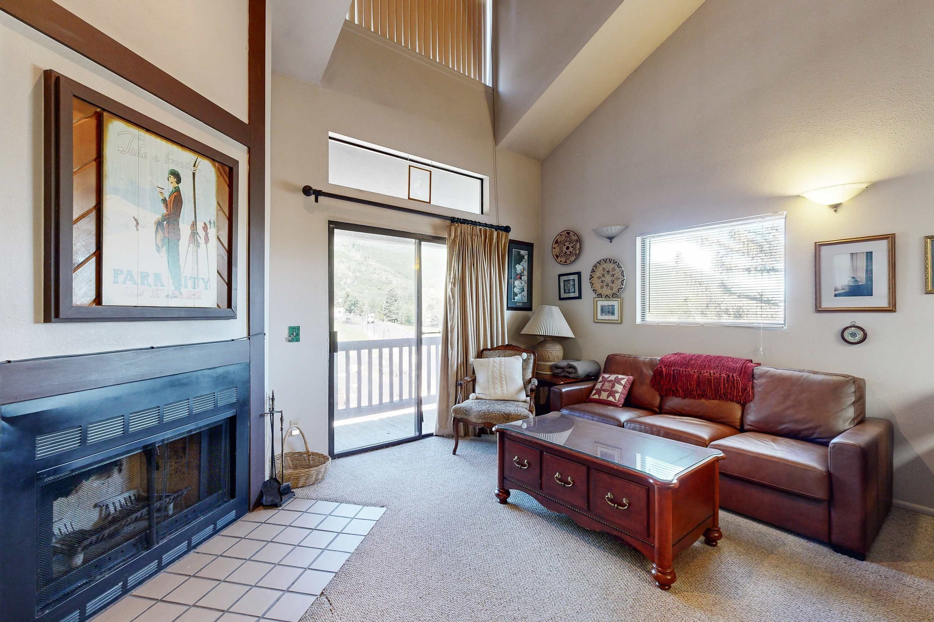 A living room with a fireplace, a sofa, a coffee table, and a sliding glass door leading to a balcony.