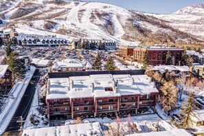 A multi-story hotel with a snow-covered roof, a parking lot, and a ski resort in the background. - Stunning views, Pool & Hot Tub, gas grill (Park City)