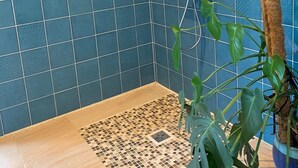 Et badeværelse med blå mønstrede fliser, en bruser med håndbruser, en bambusplante og et mosaikgulv.