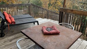 En træterrasse med et bord og stole, en loungeseng med rød pude, og et trægelænder.