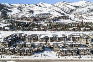 Une station de ski enneigée, avec des bâtiments à plusieurs étages, des pistes de ski et un paysage montagneux en arrière-plan.