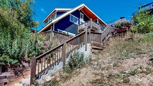 A house with a wooden staircase leading to a deck, surrounded by natural vegetation. - Upper-level home near Main St with private hot tub, deck, ski & mtn views (Park City)