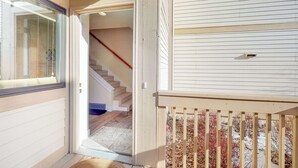 Ein Flur mit einer Holztreppe, einer Tür zu einem Zimmer und einem Fenster mit Jalousien.