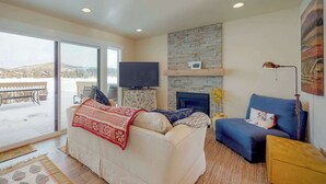 Ein Wohnzimmer mit einer Couch, einem blauen Sessel, einem Fernseher, einem Kamin und einem großen Fenster.